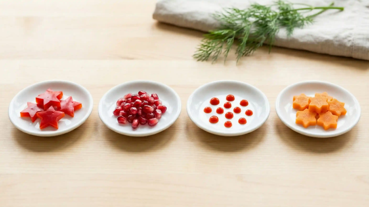 Small white plates with neatly arranged red and orange garnishes including star-cut vegetables, pomegranate seeds, hot sauce dots, and carrot stars.